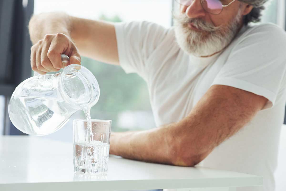 Un senior est en train de boire un verre d'eau afin de lutter naturellement contre les douleurs aux reins
