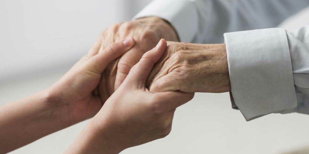 Une personne réconfortant un senior face au décès de sa femme. Il pourra prétendre à l'aide ASIR.