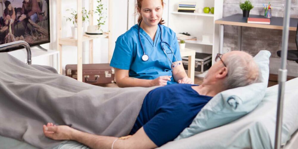 Un homme senior bénéficiant de l'ARDH avec son médecin à domicile, dans son lit médicalisé
